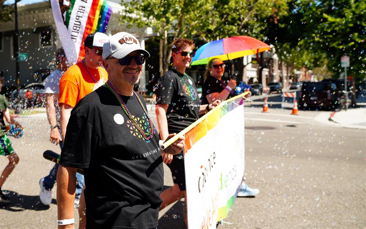 Employees hold a banner displaying the Cadence company name with a rainbow band across the top.