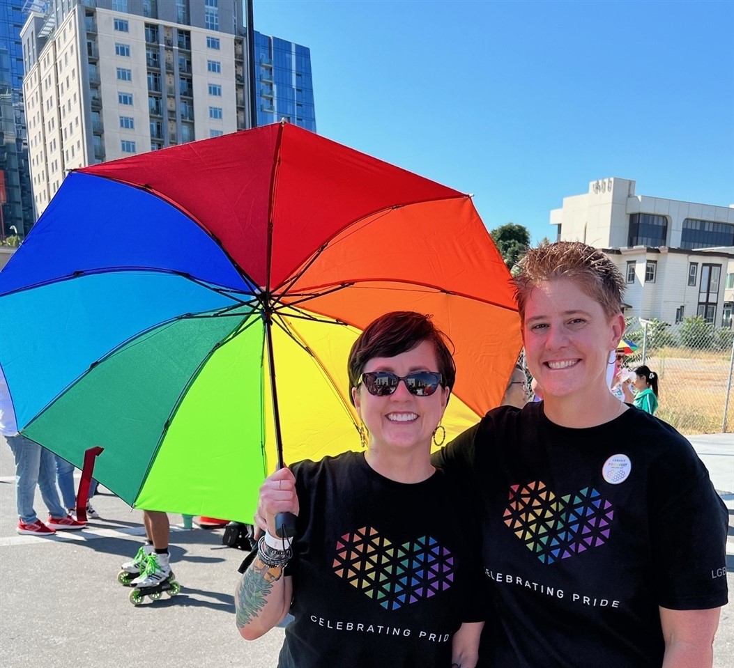 Two woman are smiling with a colorful umbrella on a sunny day.